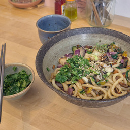 A bowl of noodles on a table with a smaller bowl with fresh coriander beside it.
