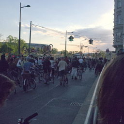 A city road filled with people on bikes, currently idling. Some of them lift their bikes up in the air.