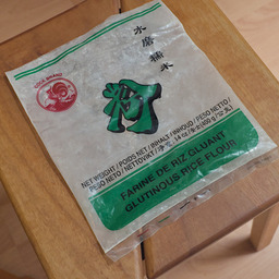 An empty bag of rice flour on a wooden stool. It has a red rooster as a logo on it that proudly states "Cock Brand" on top of it.