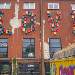 A rusty metal plated wall that carries large cut out letters spelling LOVE. The space of each letter is filled with differently colored and shaped bird houses.