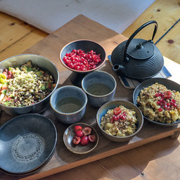 A breakfast consisting of homemade vegan porridge topped with cherries, pomegranate seeds, tea and a beansalat with cucumbers, carrots, avocado pieces, roasted seeds and freshly sprouted mung beans.