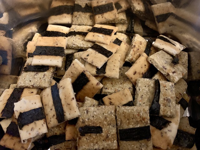 A close up shot of a metal box filled with little square crackers with a strip of nori on each.