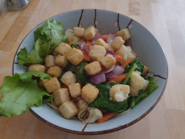 A bowl filled with broiled veggies and crispy pieces of fried tofu.