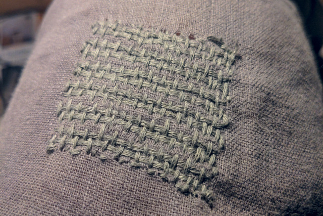 A closeup of a gray textile with a neatly patched hole in the same color.