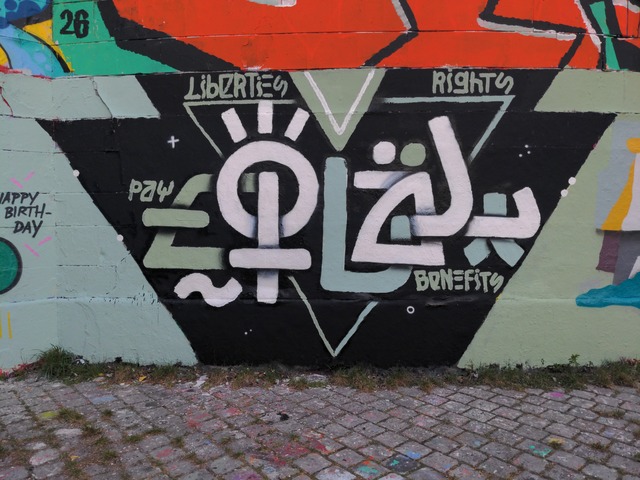 A mural showing the word EQUAL in bold, semi-abstract letters. Around it are four smaller words: PAY, RIGHTS, BENEFITS, LIBERTIES