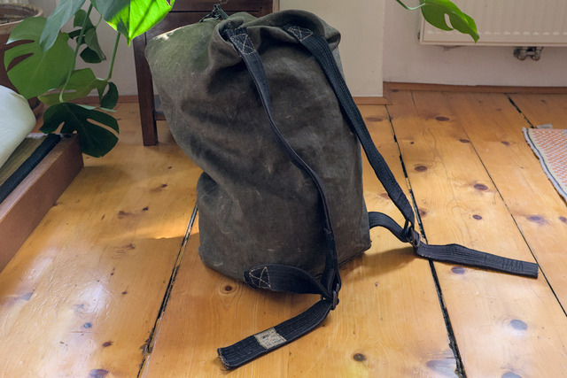 A olive green kitbag made of heavy linen and cotton with two broad straps sewn on.