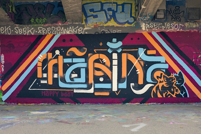 A wall with a large painting reading the letters MARINA as well as two bumbly cats licking each other.