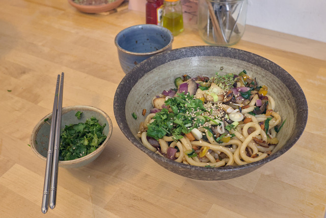 A bowl of noodles on a table with a smaller bowl with fresh coriander beside it.