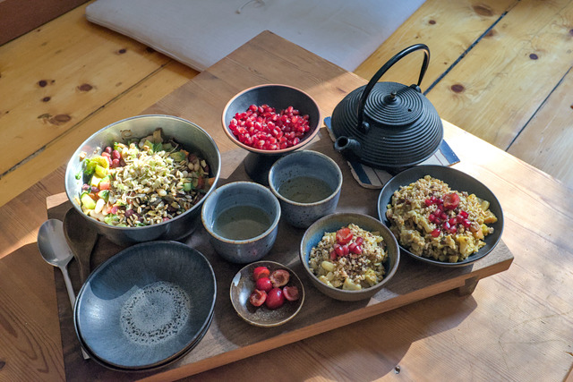 A breakfast consisting of homemade vegan porridge topped with cherries, pomegranate seeds, tea and a beansalat with cucumbers, carrots, avocado pieces, roasted seeds and freshly sprouted mung beans.