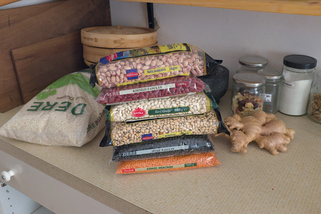 Six bags worth ~5kg of differently shaped, sized and colored beans on a kitchen counter. Next to it is a 5kg bag of rice as well as a fairly large piece of ginger root.