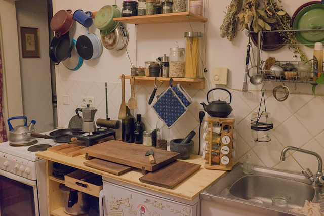 A view on a slightly crowded kitchen with a wooden cupboard between a stove and a refreigerator.